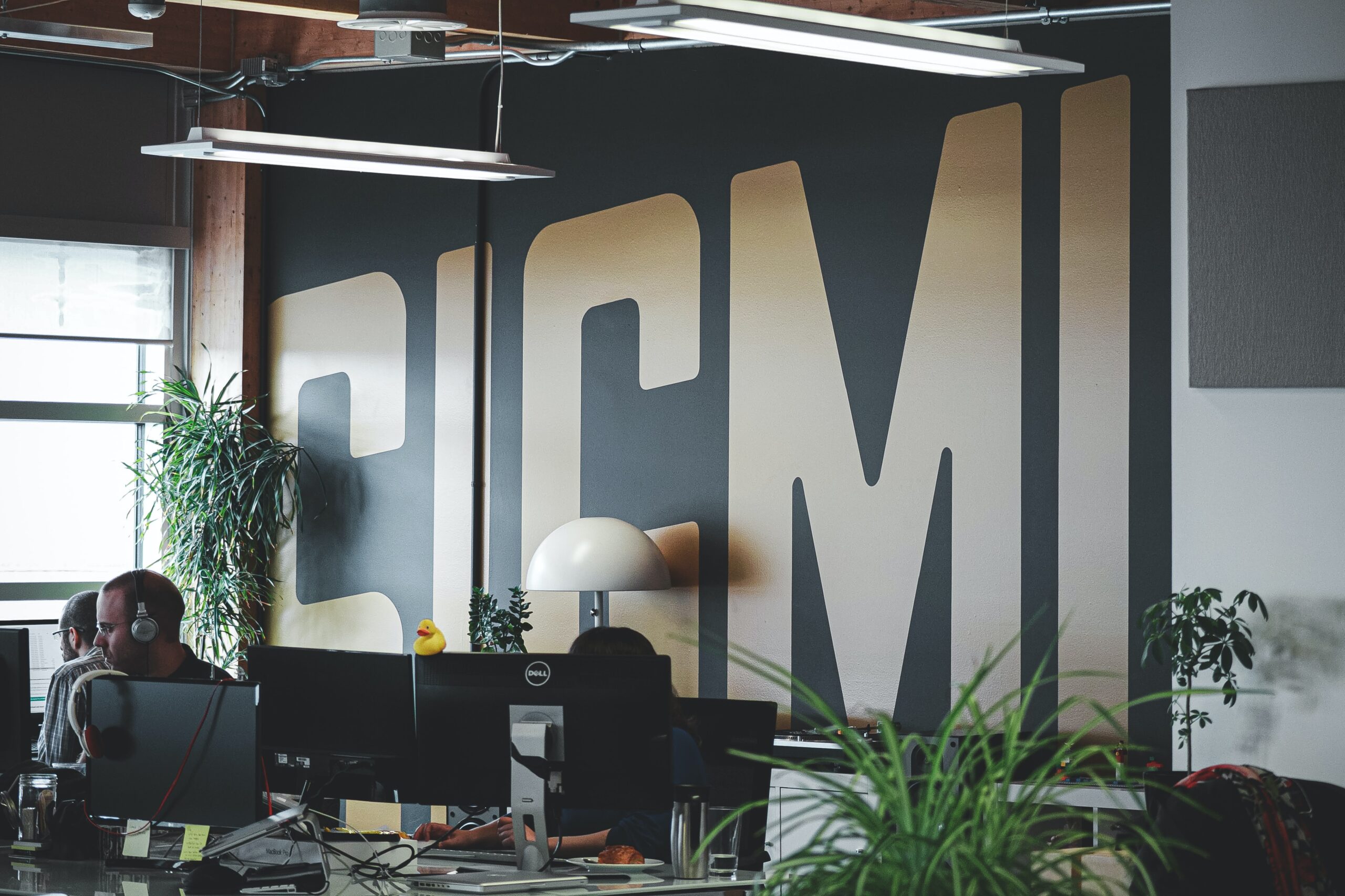 office plants and computers next to large wall sign saying sigmi