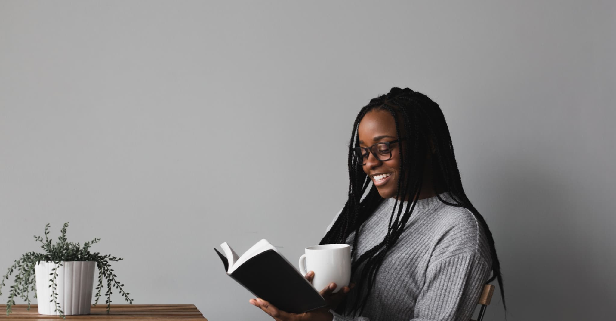 A woman reading a book while sitting at a table, smiling at something she is reading